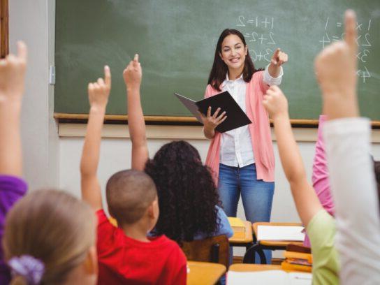 photo of teacher in front of class with students with raised hands